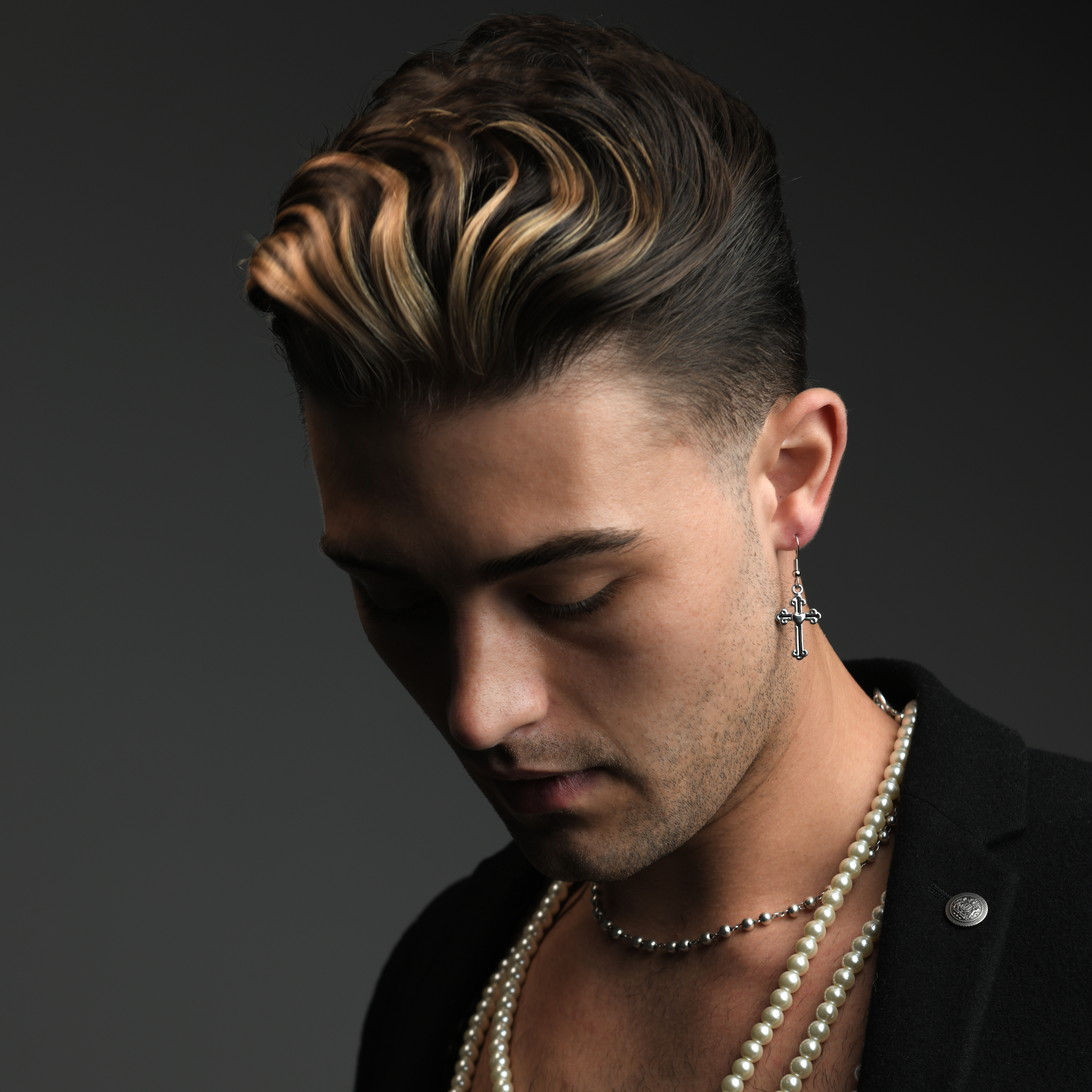 Male model wearing beaded pearl chain with wavy highlighted hair with tapered neck and sides cut with Andis clippers.
