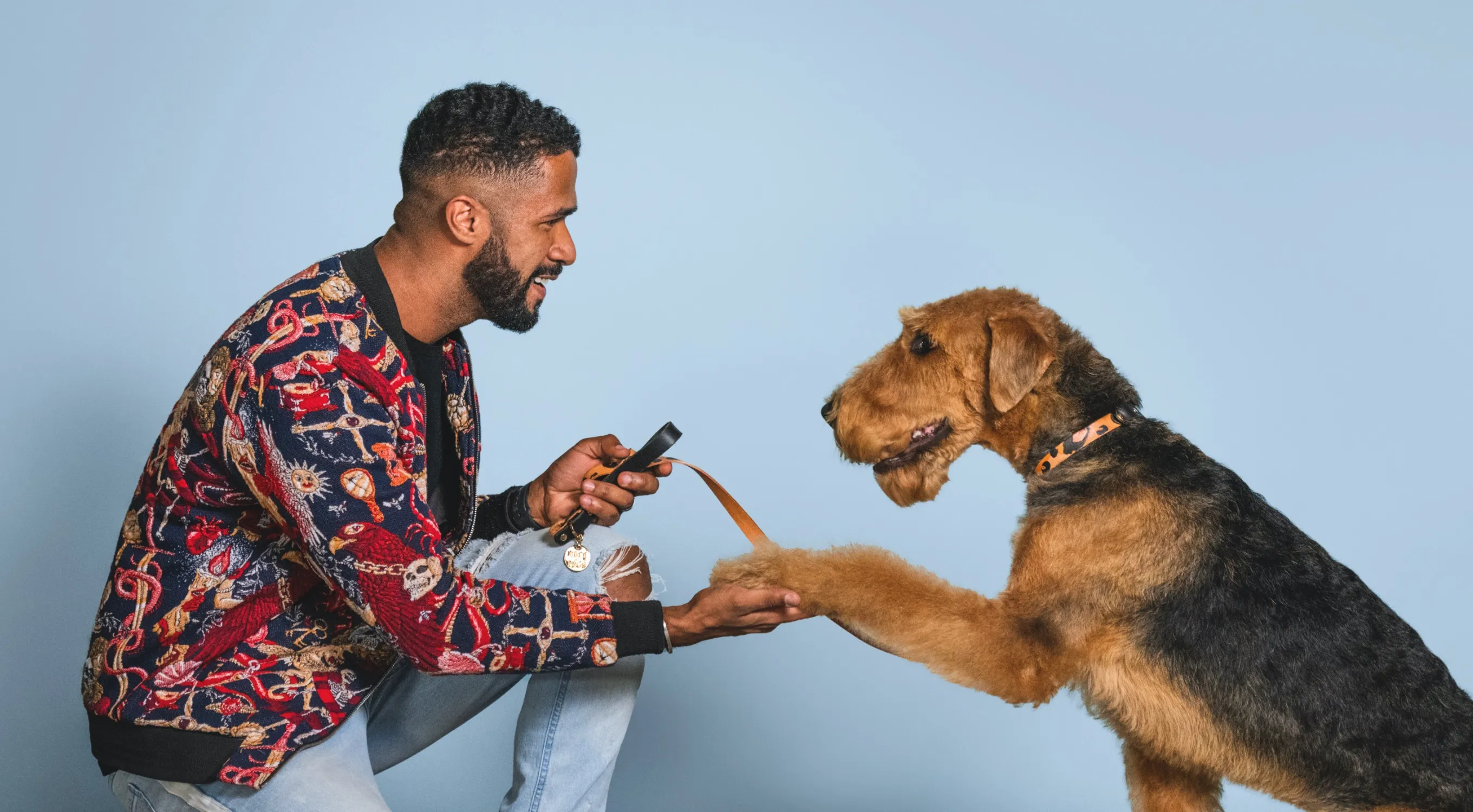 Large image of Man bent down shaking a dogs paw